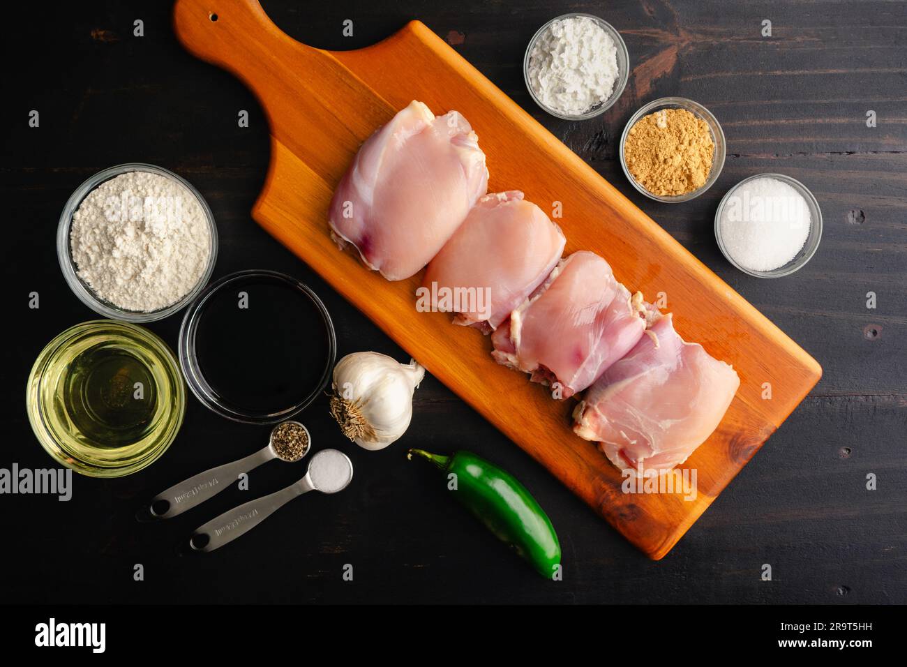 Knusprige hawaiianische Knoblauch-Hühnchen-Zutaten auf dunklem Holz Hintergrund: Rohe Hähnchenschenkel, Sojasauce, gemahlener Ingwer und andere ungekochte Zutaten Stockfoto