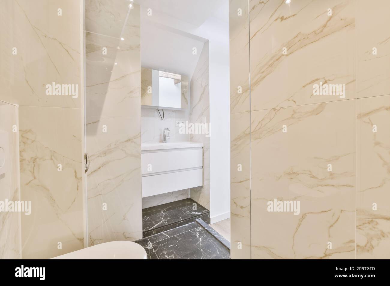 Ein modernes Badezimmer mit Marmorboden und Wänden in neutralen Farben, einschließlich einer offenen Duschkabine auf der rechten Seite Stockfoto