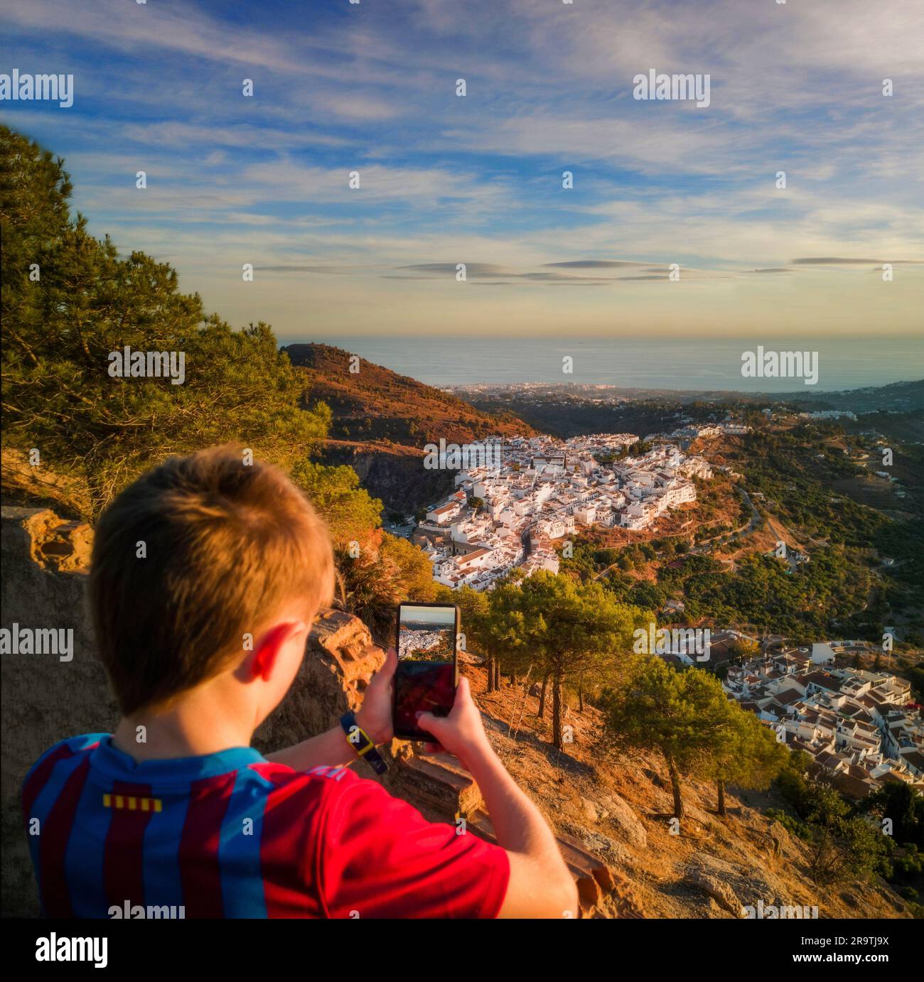 Junger Junge, der mit dem Smartphone Frigiliana Village von oben fotografiert, Malaga Province, Andalusien, Spanien Stockfoto