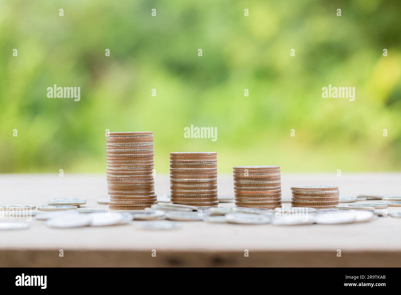 Geldmünzen stapeln sich auf einem Holzschreibtisch mit grünem Hintergrund. Management-Bargeld, Versicherungsvermögen und Vermögen, Steuerbudget, Wachstumsdarlehen, Wirtschaft Stockfoto