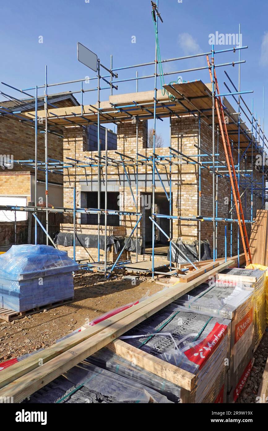 Um den neuen freistehenden Hausaufbau herum gelagerte Baumaterialien, einschließlich Dachziegeln, Holz und Dachträger, werden im Bau von Essex England UK gelagert Stockfoto