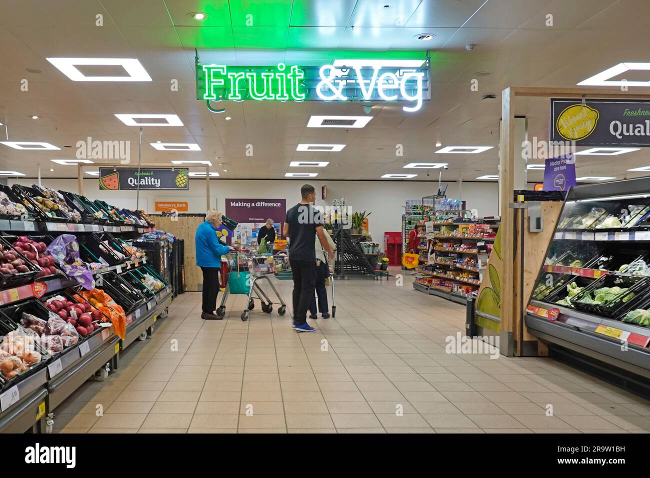 Innenansicht der Kunden, die im Fruit & Veg Department des Supermarktes Sainsburys einkaufen, mit beleuchtetem Schild Essex England UK Stockfoto