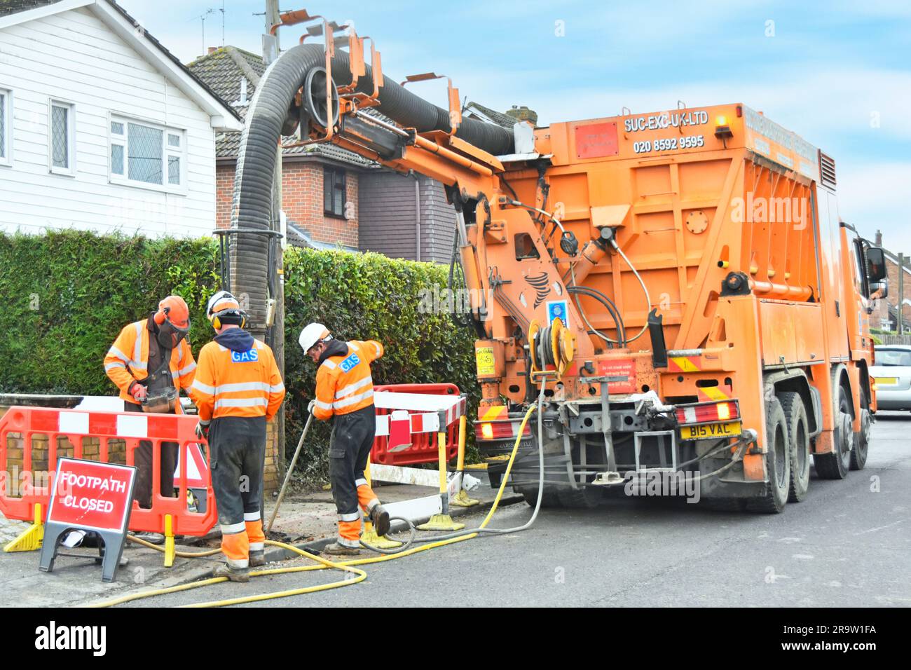 Saugbagger auf lkw-Lkw und Red-hat-Fahrer halten Fernsteuerung in Zusammenarbeit mit zwei Gasunternehmen, die den Gasanschluss in Großbritannien freilegen Stockfoto