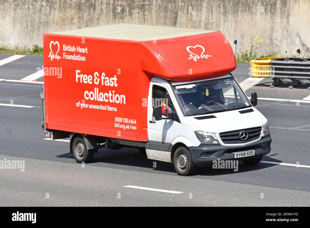 Logo der British Heart Foundation auf der Vorderseite des rot-weißen Kleinbusses für wohltätige Zwecke und des Fahrers, der auf der Autobahn M25 in der Umlaufbahn von Essex England fährt Stockfoto