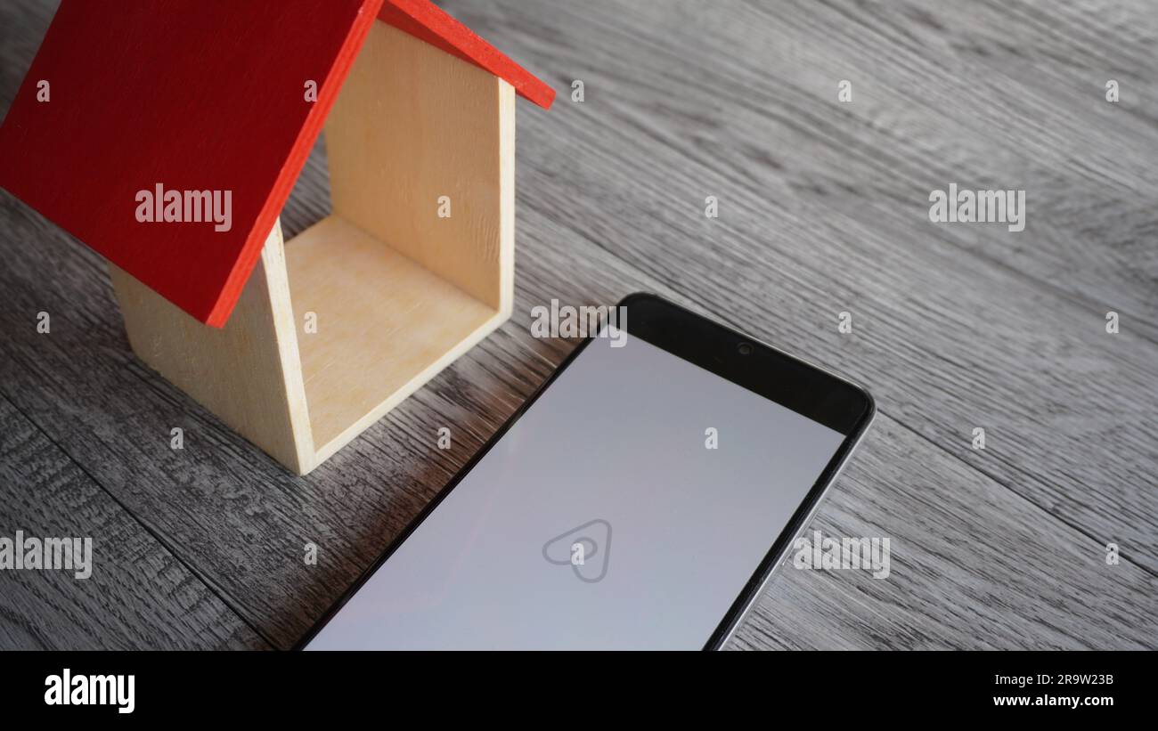 Airbnb-Logo auf Smartphone und Miniaturhaus auf Holztisch mit Kopierbereich Stockfoto