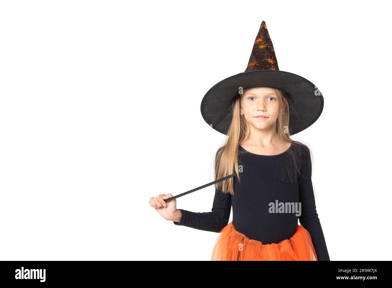 Kinder An Halloween. Ein hübsches, süßes Mädchen in einem Hexenkostüm, trägt einen Hut und einen Zauberstab auf einem Studio mit weißem Hintergrund, Kopierraum. Der kleine Ssor Stockfoto