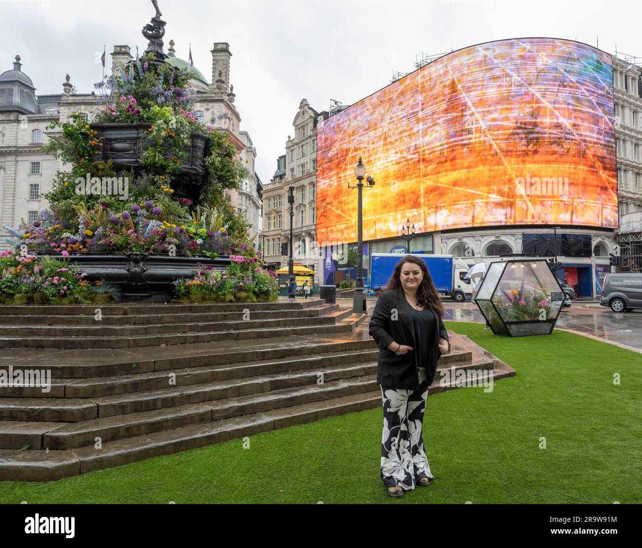 Piccadilly Circus, London, Großbritannien. 29. Juni 2023. Art of London feiert die Rückkehr von Art After Dark mit einer neuen, beleuchteten öffentlichen Kunstattraktion, die den Piccadilly Circus für zwei Tage verwandelt. Der Shaftesbury Memorial Fountain wurde mit Tausenden von Blumen dekoriert und beruhigende Videokunst wird auf die Piccadilly Lichter projiziert, da über 40 Kunstgalerien am Donnerstag, den 29. Und Freitag, den 30. Juni, für das zweitägige Kulturprogramm geöffnet sind. Bild: Visuelle Künstlerin Amelia Kosminsky neben der Installation und Piccadilly Lights als Videobildschirme. Kredit: Malcolm Park/Alamy Live News Stockfoto