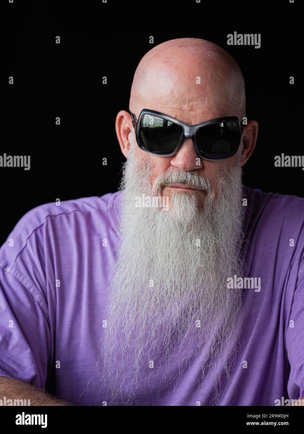 Porträt eines Mannes mit langem grauem Bart, der ein lilafarbenes T-Shirt und eine Sonnenbrille im Nahaufnahme-Porträt trägt Stockfoto