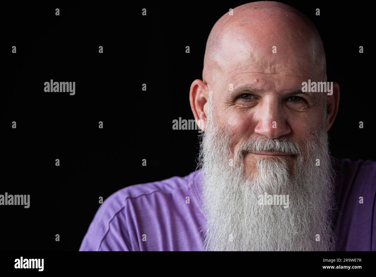 Porträt eines Mannes mit langem grauem Bart, der ein lilafarbenes T-Shirt im Nahaufnahme-Porträt trägt Stockfoto