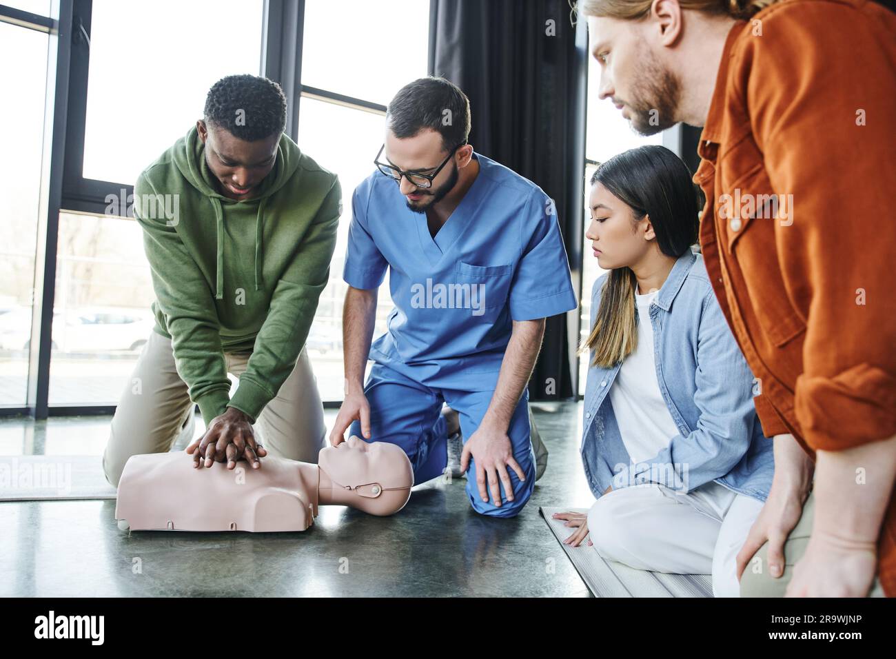 Junge multiethnische Menschen und medizinischer Lehrer, der einen afroamerikanischen Mann ansieht, der Thoraxkompressionen an der HLW-Prüfpuppe durchführt, kardiopulmonale Reanimation Stockfoto