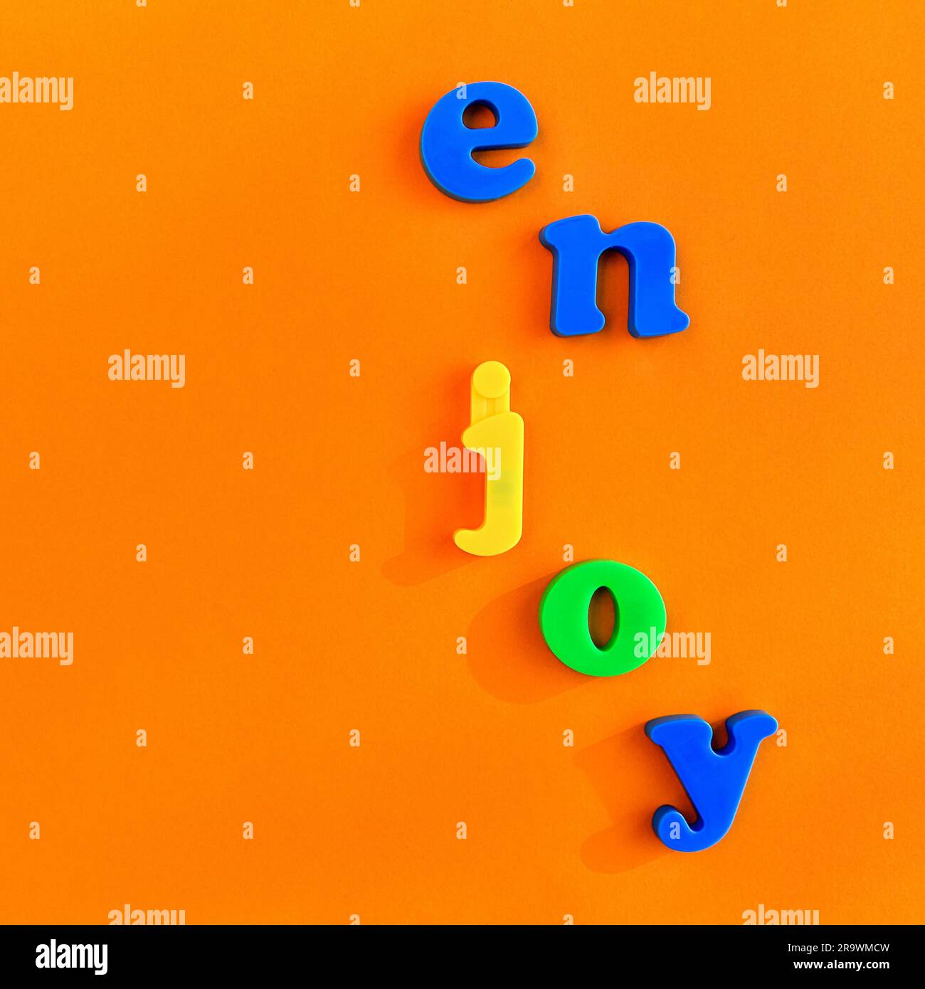 Farbenfrohe Buchstaben bilden das Wort Genießen, vertikale Anordnung, Tischplatte, minimalistisch, Symbolbild Genießen Sie Spaß Stockfoto