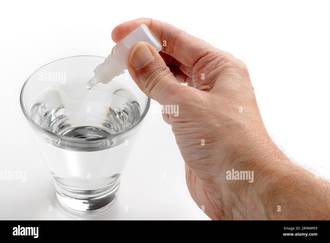 Die Hand des Menschen setzen Apotheke Tropfen in ein Glas transparent Wasser auf weißem Hintergrund Stockfoto