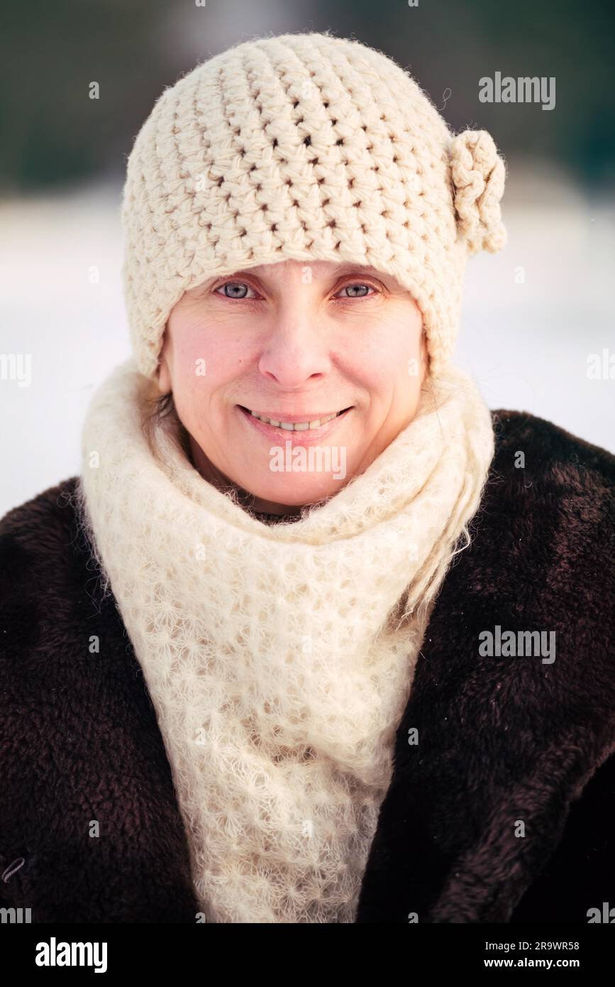 Ein Winter-Porträt einer lächelnden senior Erwachsene Frau trägt eine Mütze und einen Schal mit einem Schnee-Hintergrund Stockfoto
