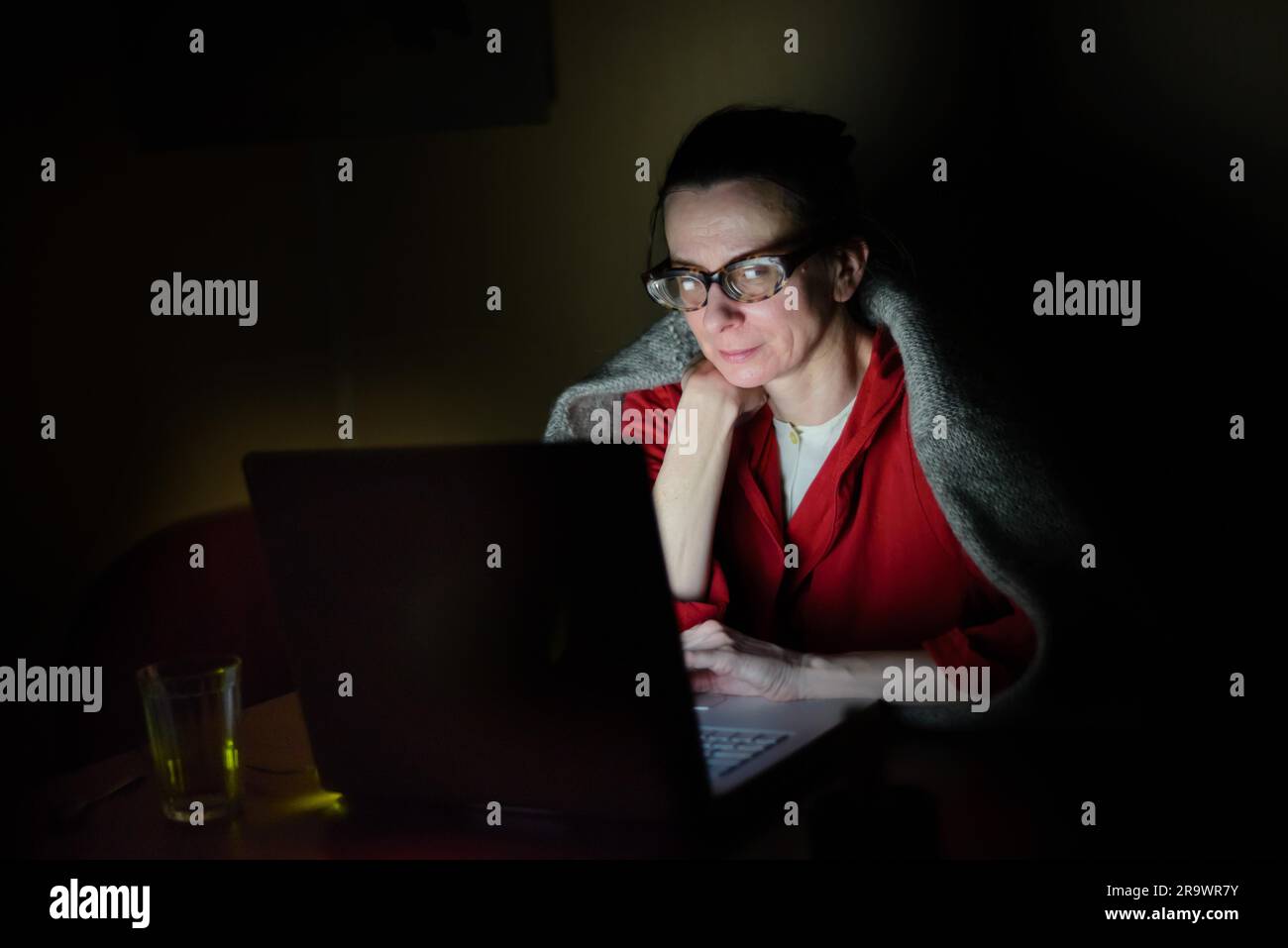 Eine ältere Frau, die an einem kalten Winterabend im Dunkeln einen Computer benutzt Stockfoto