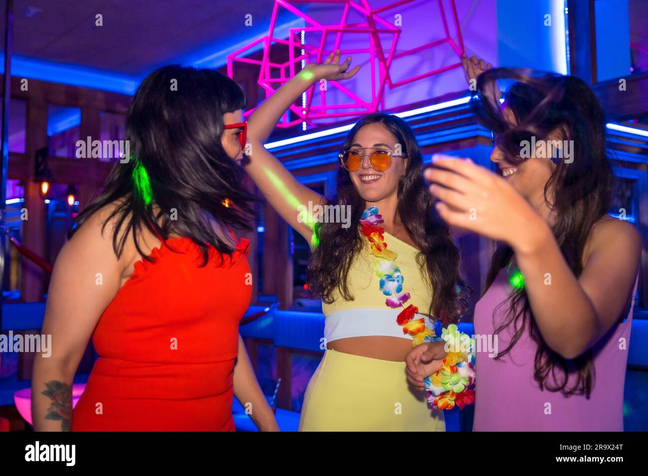 Weibliche Freunde in einer Disco, die lächelnd auf einer Nachtparty in den Sommerferien in einem Pub tanzen Stockfoto