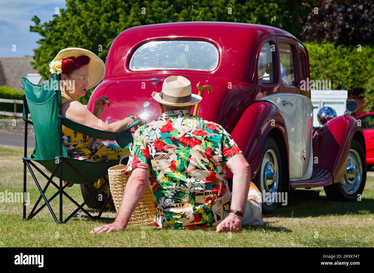 Mann und Frau in den Vintage 1940er und 1950er Jahren Kleidung auf dem Gras neben Einem klassischen Oldtimer, Christchurch England, Großbritannien Stockfoto