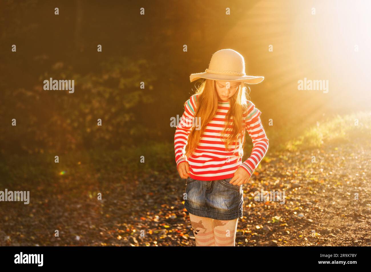 Außenporträt eines hübschen Mädchens mit großem Hut, pinkfarbenem gestreiftem Pullover und Denimrock Stockfoto