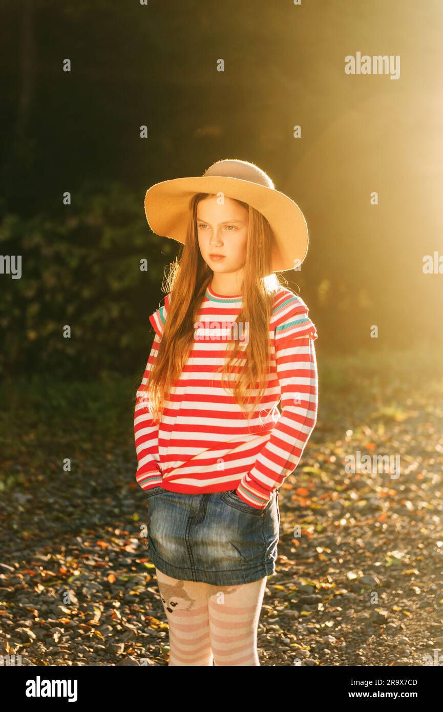 Außenporträt eines hübschen Mädchens mit großem Hut, pinkfarbenem gestreiftem Pullover und Denimrock Stockfoto