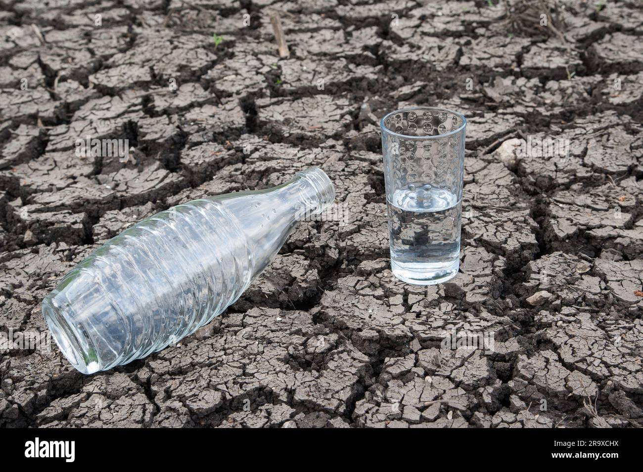 Die leere Wasserflasche symbolisiert Wasserknappheit, während das halbvolle Glas Trinkwasser Hoffnung vermittelt. Stockfoto