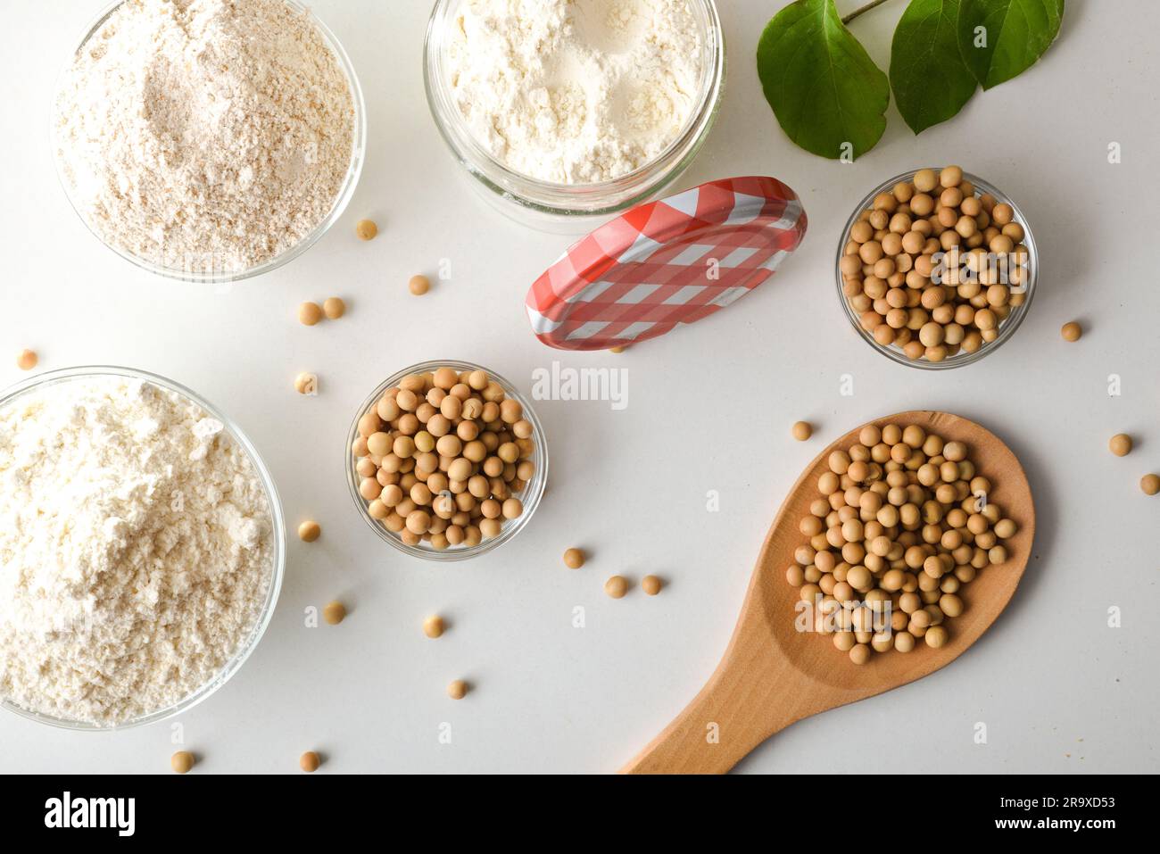 Details des ganzen und raffinierten Sojabohnenmehls auf einer weißen Küchenbank mit Glasschüsseln gefüllt mit Getreide und Mehl. Draufsicht. Stockfoto