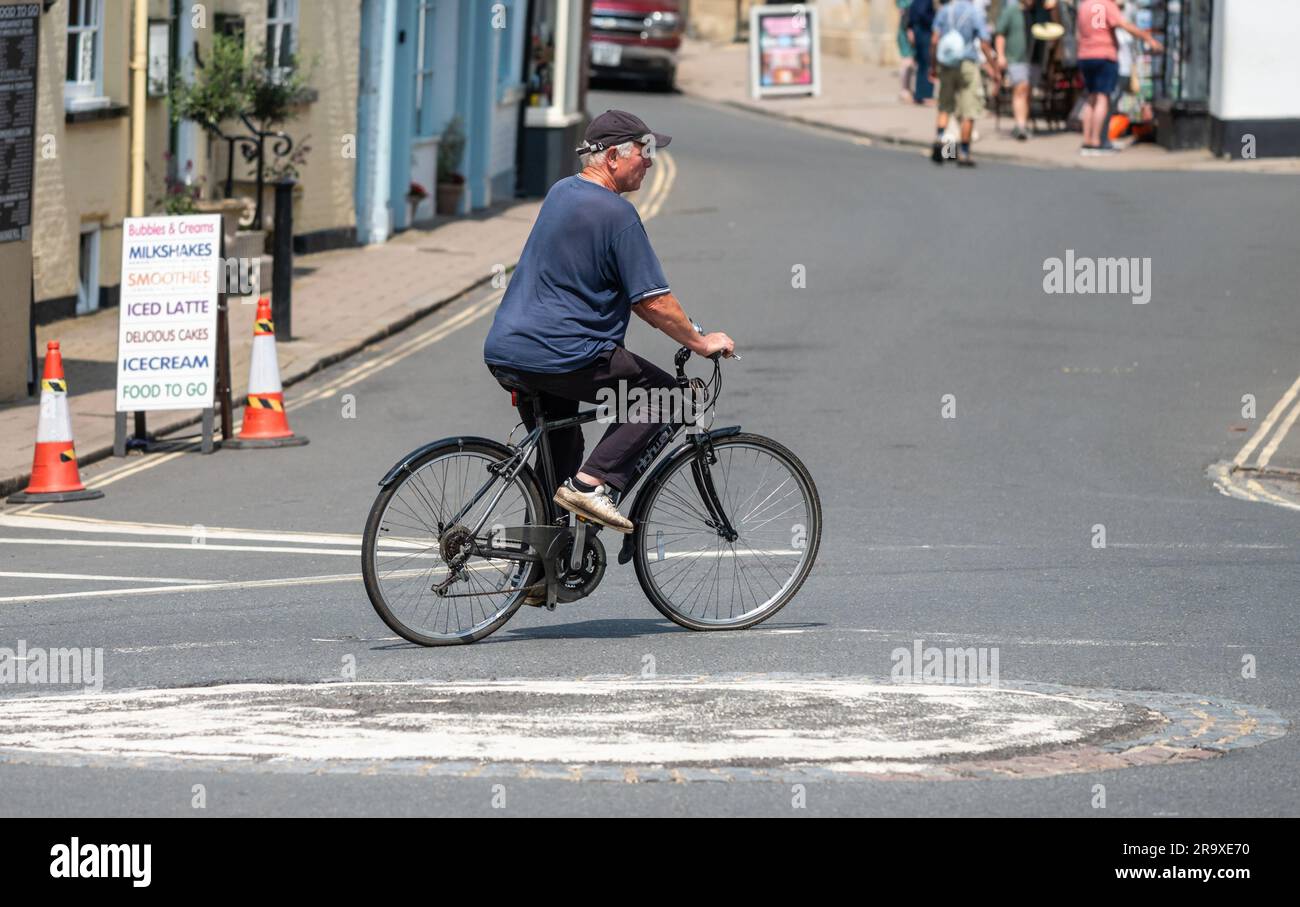 Männlicher Radfahrer in Summer, der auf einem Fahrrad um einen kleinen Kreisverkehr auf einer britischen Straße in England fährt. Stockfoto