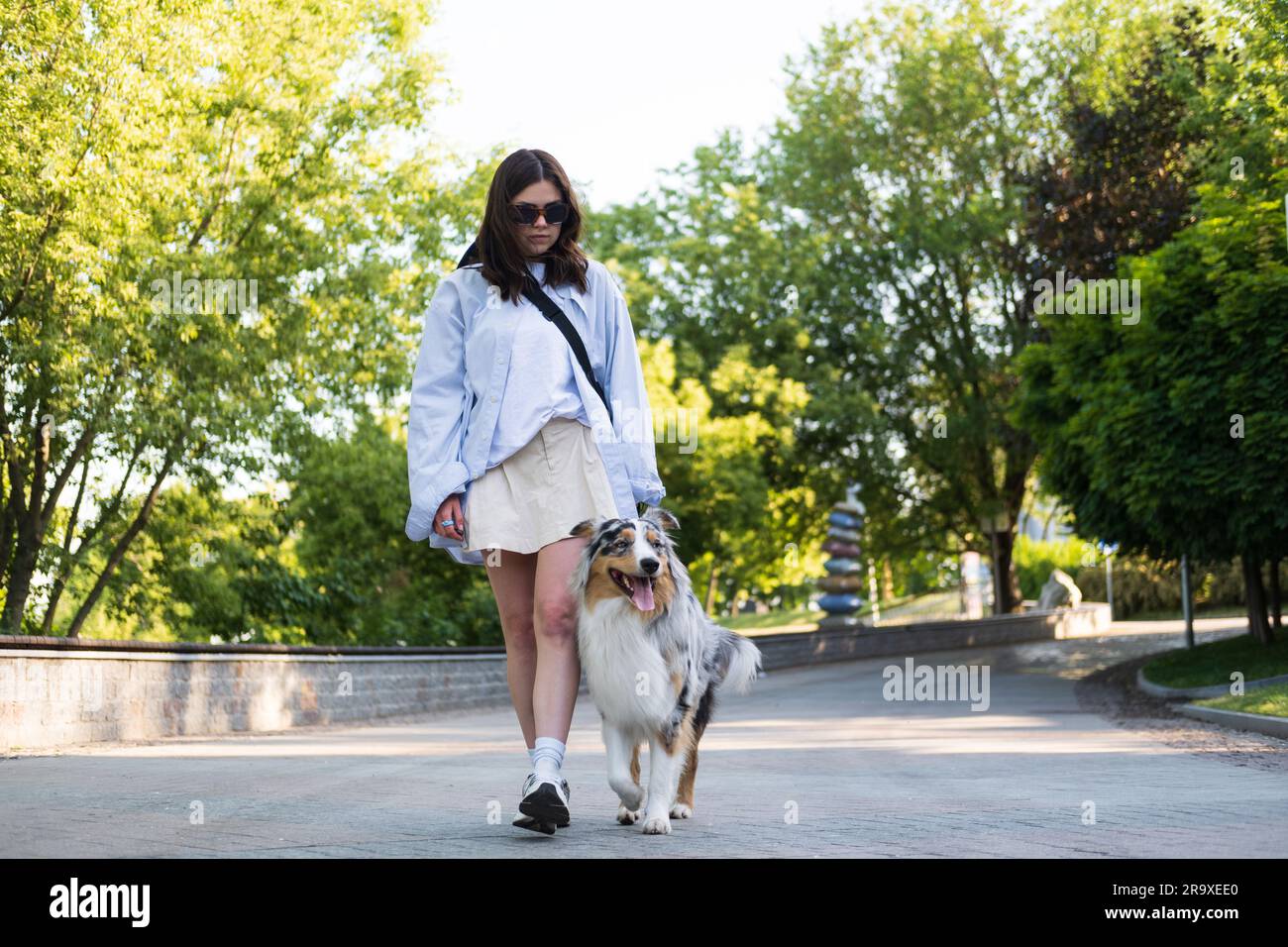 Junge Frau führt ihren australischen Hund in einer städtischen Gasse aus und verbringt Zeit mit Haustieren im Freien. Mitte 20s mit australischem Schäferhund an der Leine Stockfoto