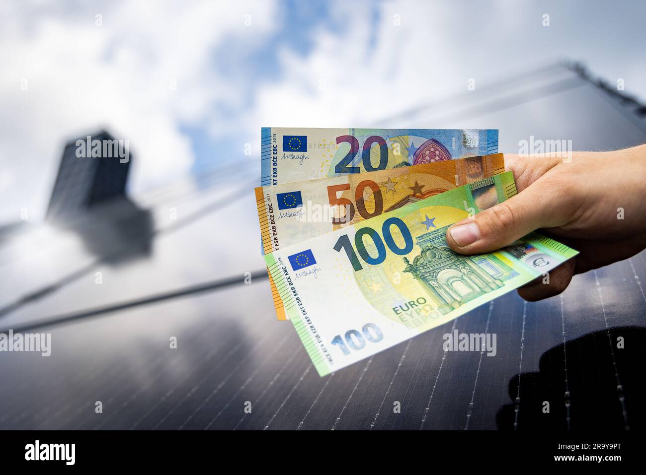 Euro-Banknoten in einer Hand mit einem Sonnenkollektordach im Hintergrund Stockfoto