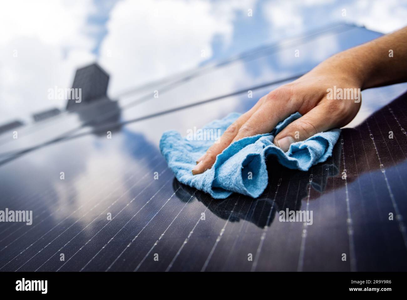 Nahaufnahme einer Hand, die einen Sonnenkollektor mit einem Tuch reinigt Stockfoto