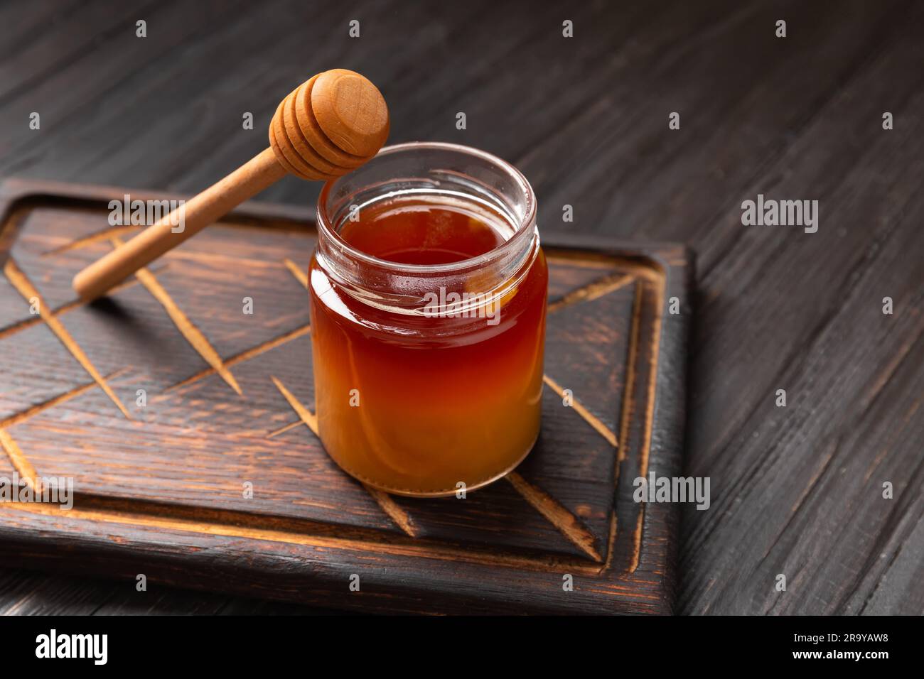 Honig in einem Becher und ein Holzdipper auf einem dunklen Holzbrett auf einem strukturierten Hintergrund. Buchweizenhonig auf dunklem Hintergrund. Stockfoto