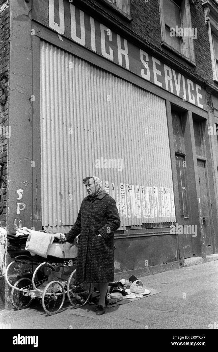 Poverty London 1970er Vereinigtes Königreich. Eine arbeitslose Frau verkauft alte Kleidung und Schrott von Kinderwagen, um ihr armes Leben zu vervollständigen. Sie steht vor einem Laden, der geschlossen hat. Rufen Sie den Quick Service an. Whitechapel, London, England, ca. 1972 70s HOMER SYKES Stockfoto