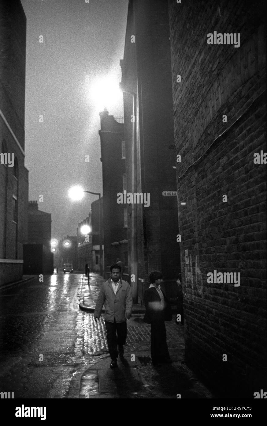 Victorian Slum Buildings East End London 1970er Jahre, Brick Lane an der Kreuzung mit Sheba Street. Ein asiatischer Mann und ein Teenager laufen vorbei an den viktorianischen Wohnblöcken. Tower Hamlets, London, England 1976. HOMER SYKES AUS DEN 70ER JAHREN Stockfoto