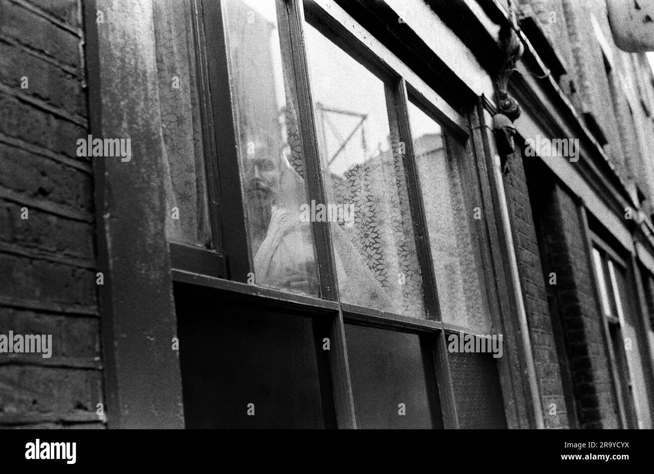 Whitechapel London in einer Straße in der Nähe der Brick Lane starrt eine einsame Asiatin aus ihrem Flachfenster. In der Presse war berichtet worden, dass viele neue Einwanderer nach Großbritannien, insbesondere Frauen aus Bangladesch, von ihren Männern unter Verschluss gehalten wurden. Sie sprachen nicht die Sprache und durften nur selten aus ihren Häusern raus. Whitechapel, London, England, ca. 1978. Stockfoto