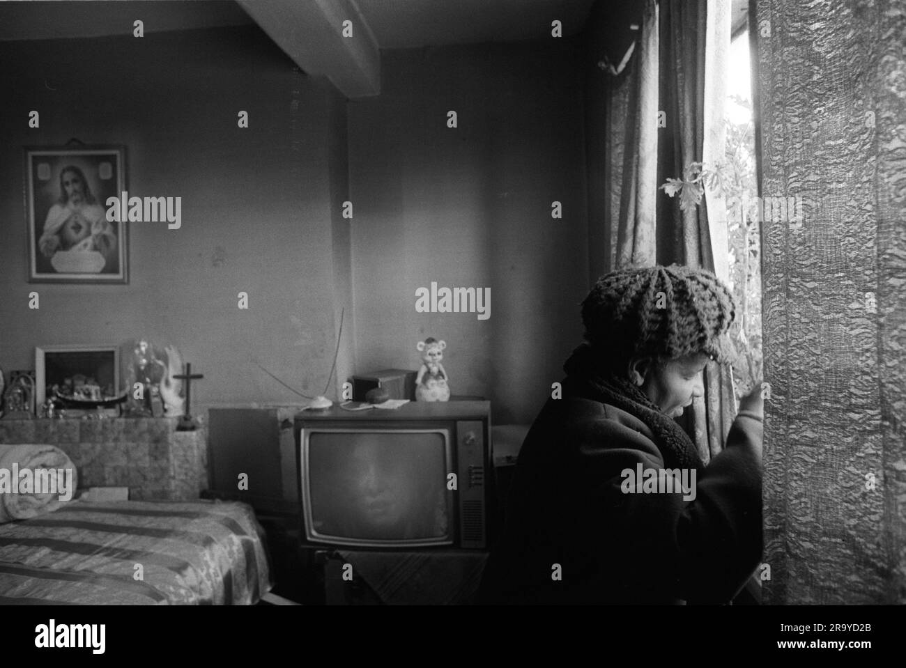 East End London 1970er UK Poverty in Britain, eine ältere schwarze britische Frau in ihrem wohnsitz auf dem Stonebridge Estate. Isoliert und allein in einem Einzelzimmer plus kleine Küche und Bad. Alles in sehr schlechtem Zustand, die Wohnung ist feucht und sehr kalt, sie trägt Hut und Mantel, um sich warm zu halten. Auf ihrem Bett ist ein "Schlafzimmer" über ihrem Bett, ein Bild von Christus. Haggerston, East London, England 1978. 70s HOMER SYKES Stockfoto