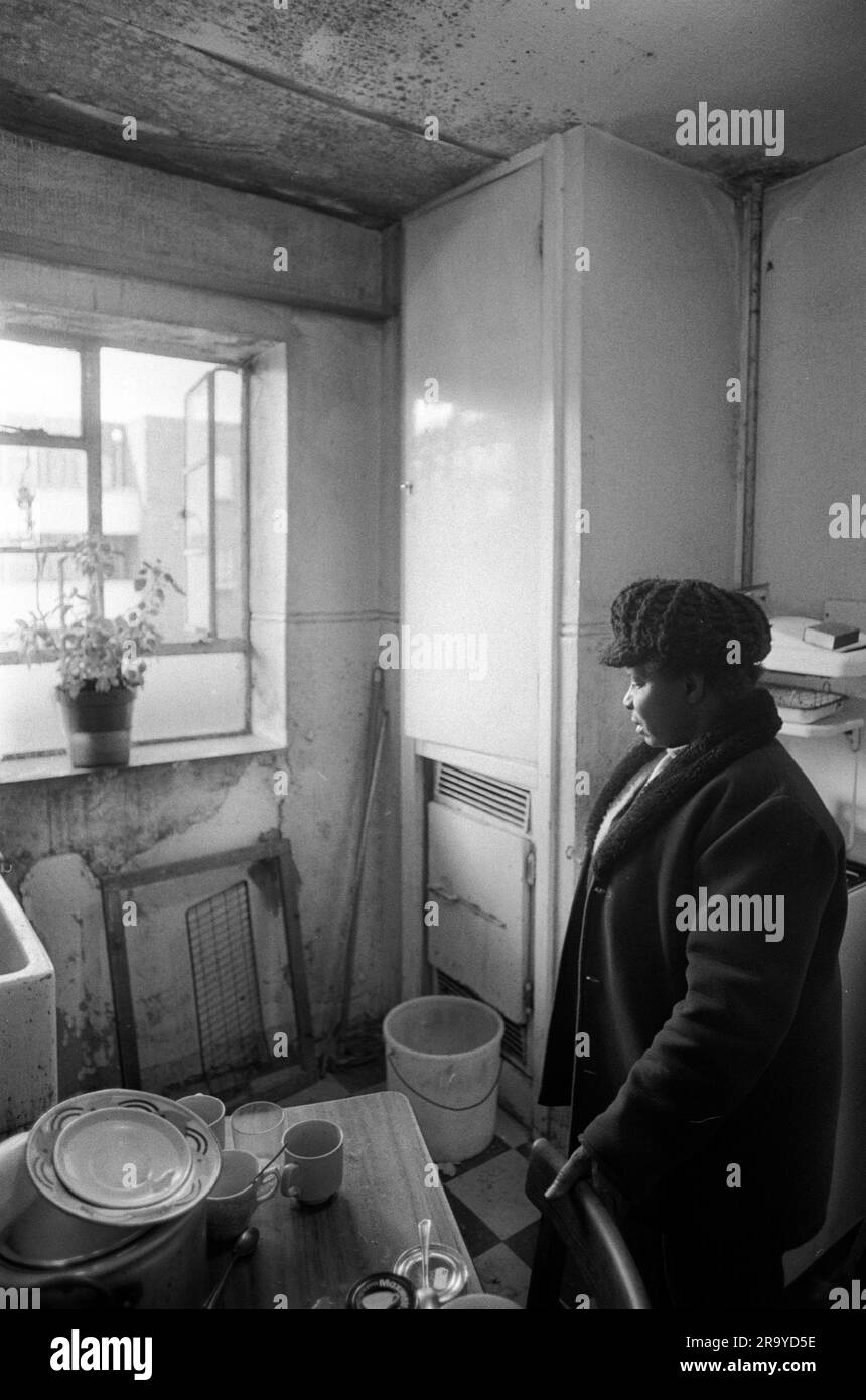 Slum der 1970er Jahre beherbergt East End London UK. Armut in Großbritannien, eine ältere schwarze britische Frau in ihrer Wohnung auf dem landsitz Stonebridge Estate. Isoliert und alleine in einem Einzelzimmer mit kleiner Küche und Bad. Alles in sehr schlechtem Zustand, die Wohnung ist feucht und sehr kalt, sie trägt Hut und Mantel, um warm zu bleiben. Haggerston, East London, England 1978. HOMER SYKES Stockfoto