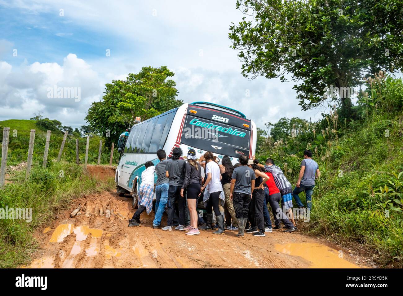 Eine Gruppe junger Leute, die einen Bus schubsen, der auf einer schlammigen Straße feststeckt. Kolumbien, Südamerika. Stockfoto