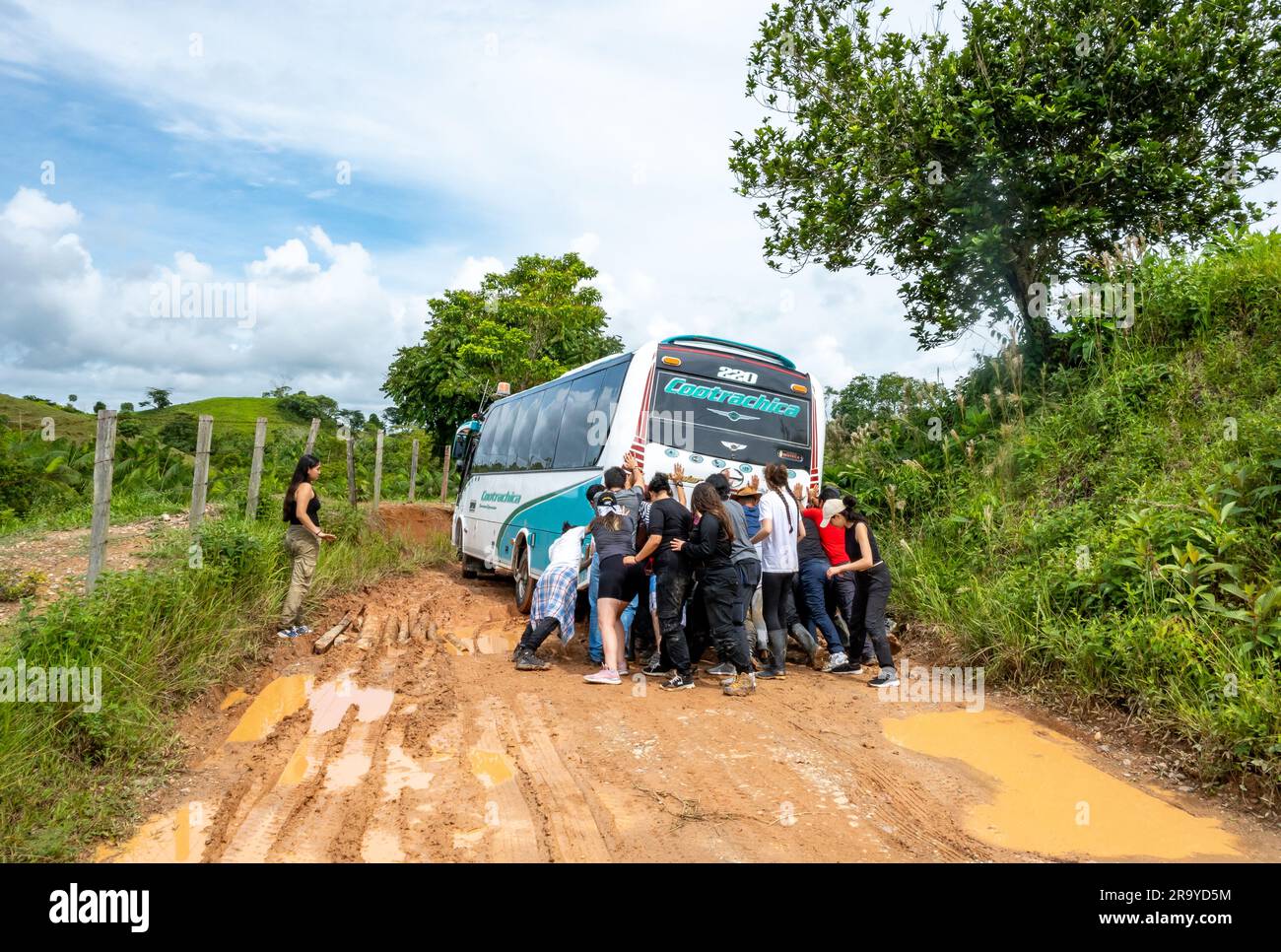 Eine Gruppe junger Leute, die einen Bus schubsen, der auf einer schlammigen Straße feststeckt. Kolumbien, Südamerika. Stockfoto