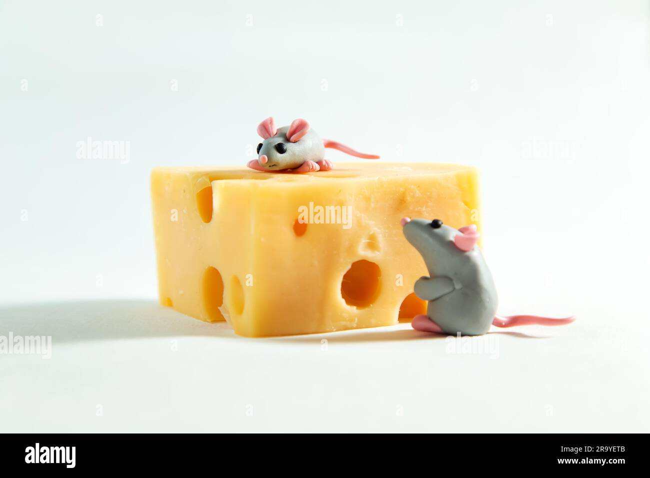 Kleine Plastikmäuse und ein Stück Käse mit Löchern. Weißer Hintergrund. Stockfoto