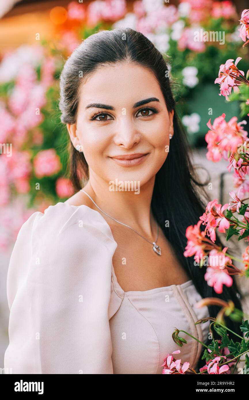 Nahaufnahme von einer schönen jungen Frau mit langem, glänzendem Haar, die sich im Freien in rosa Blumen posiert Stockfoto