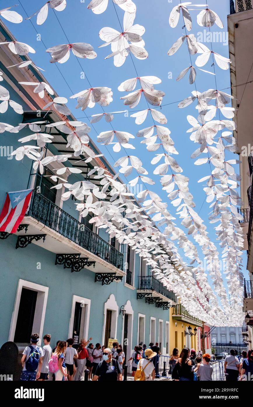 Calle Fortaleza (ehemals Schirmstraße) in der Altstadt von San Juan Puerto Rico mit weißen Schmetterlingstrainern über dem Kopf und Puerto-ricanischer Flagge über den Käufern. Stockfoto