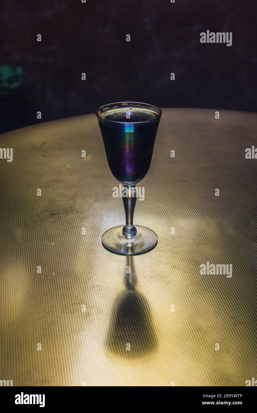 Gruseliges dunkelgraues Getränk in schillerndem Sherry-Glas auf Messingtisch bei Abendlicht Stockfoto