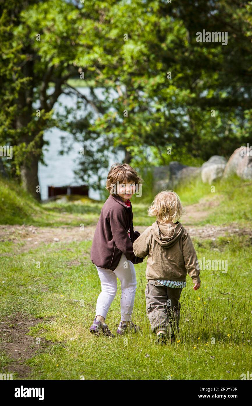 Rückansicht eines Jungen und einer Frau, die Händchen halten und auf Gras laufen Stockfoto