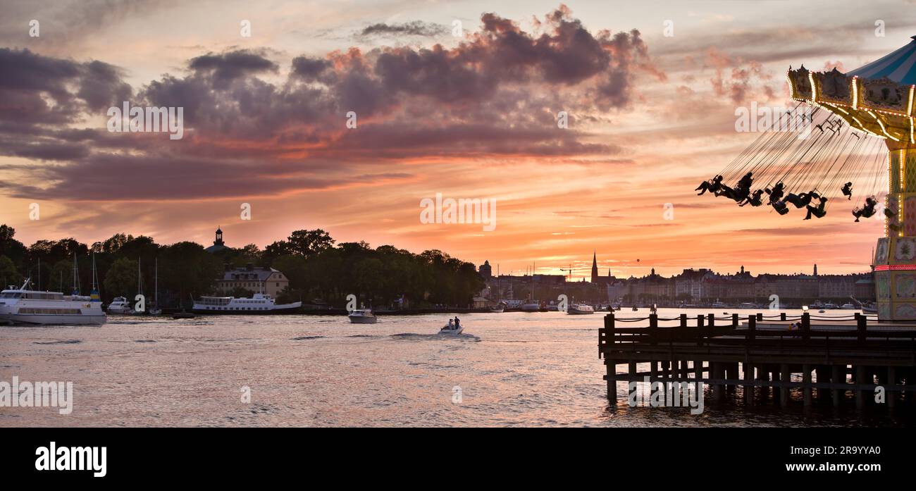 Vom Wasser aus hat man einen kurzen Blick auf das Karussell und die Silhouettenstadt im Hintergrund bei Sonnenuntergang, Gröna Lund, Stockholm, Schweden. Stockfoto