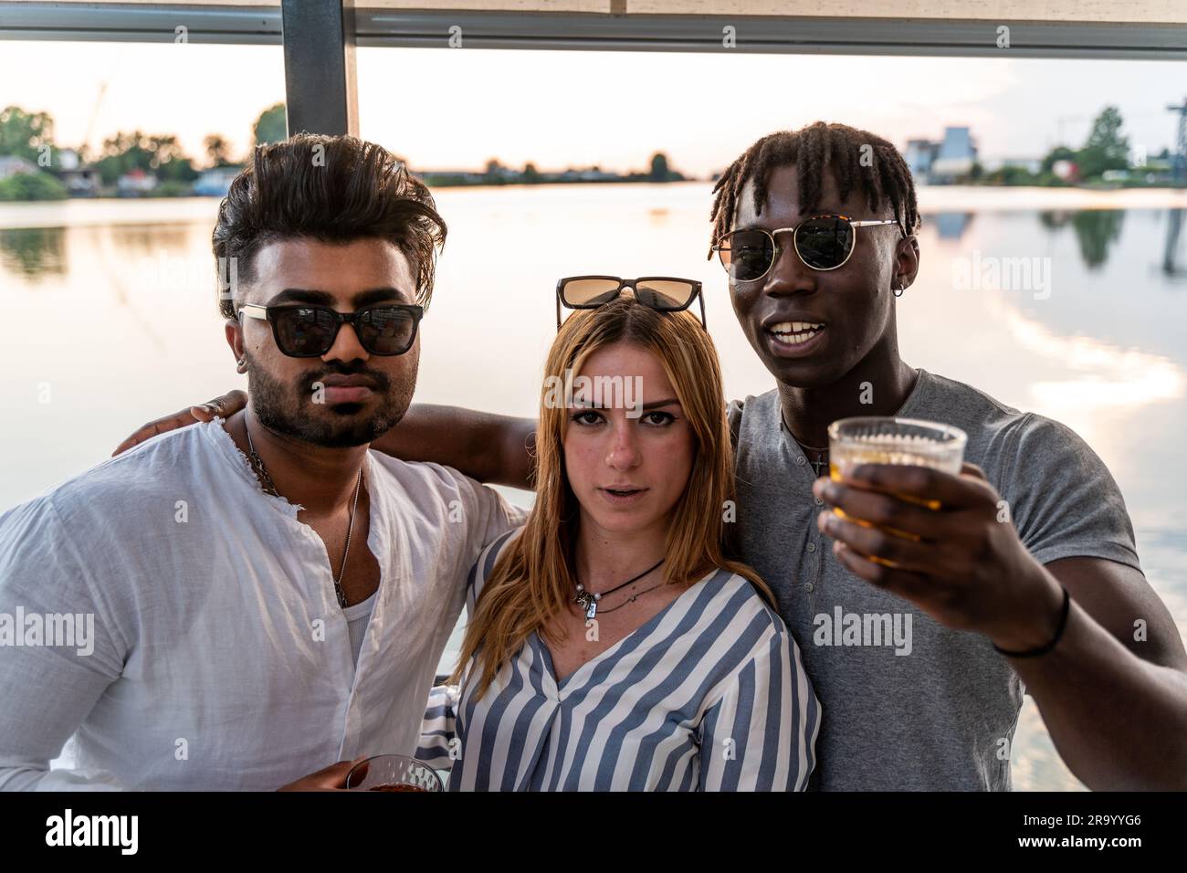 Kleine Gruppe von jungen erwachsenen multiethnischen Freunden, die mit Alkohol anstoßen - Sommerferienkonzept auf einem Schiff auf dem Fluss Stockfoto