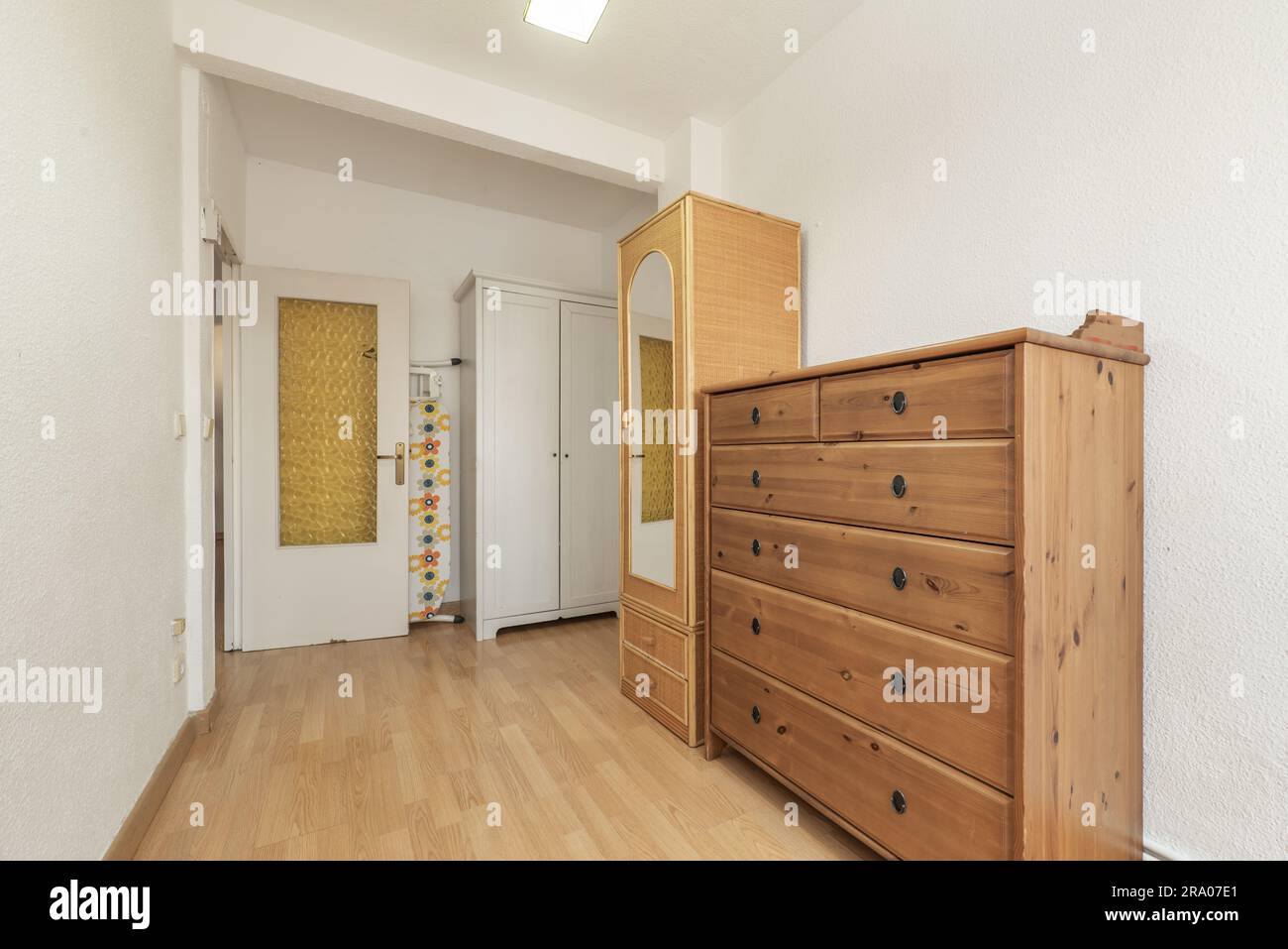 Zimmer mit einer hölzernen Seitenwand mit Schubladen, einem schmalen Korbschrank mit Spiegel und einem weißen Holzschrank Stockfoto
