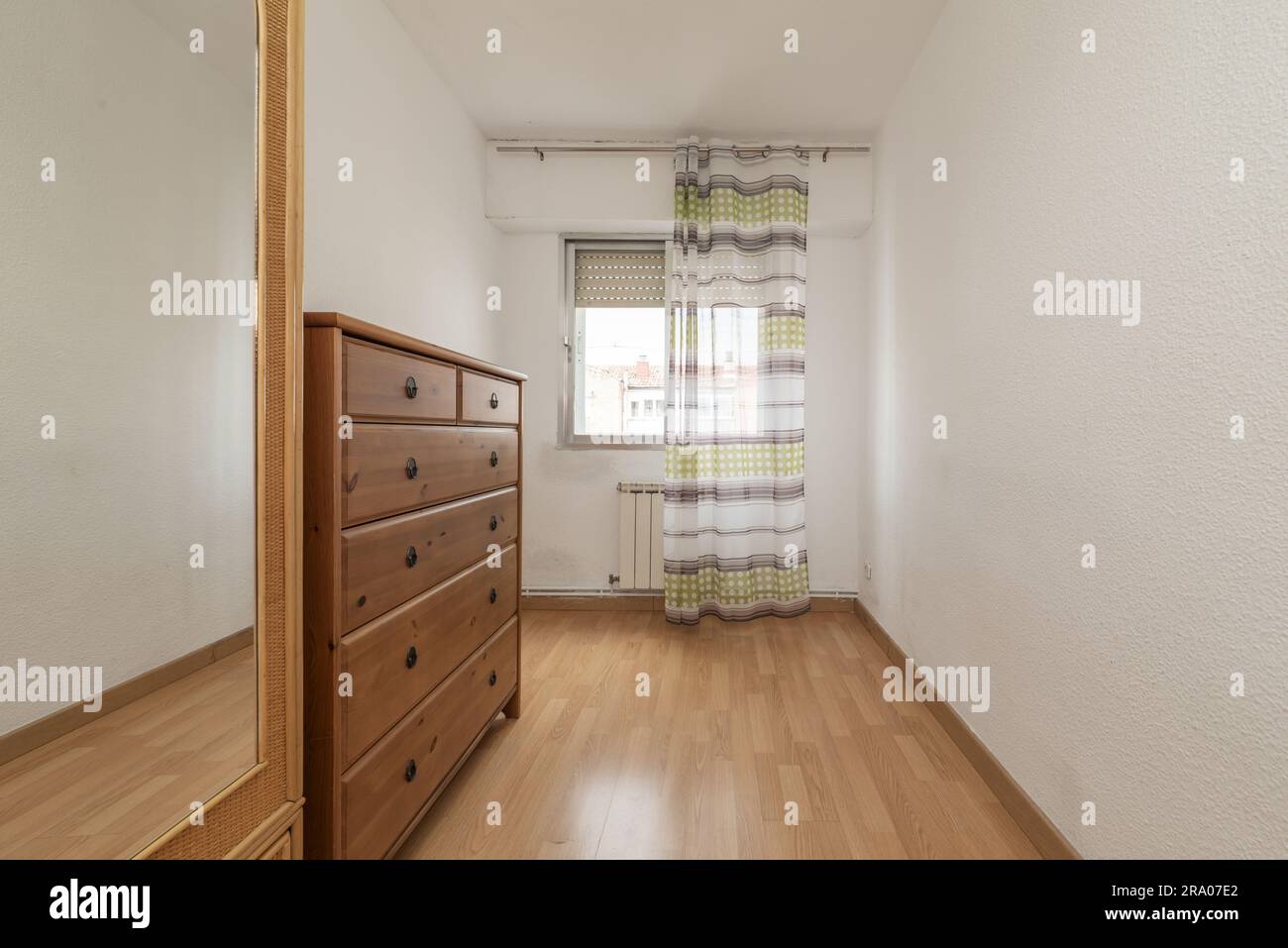 Zimmer mit einer Seitenwand aus Holzschubladen, einem schmalen Korbgarderobe mit Spiegel und einem Fenster mit Vorhängen Stockfoto