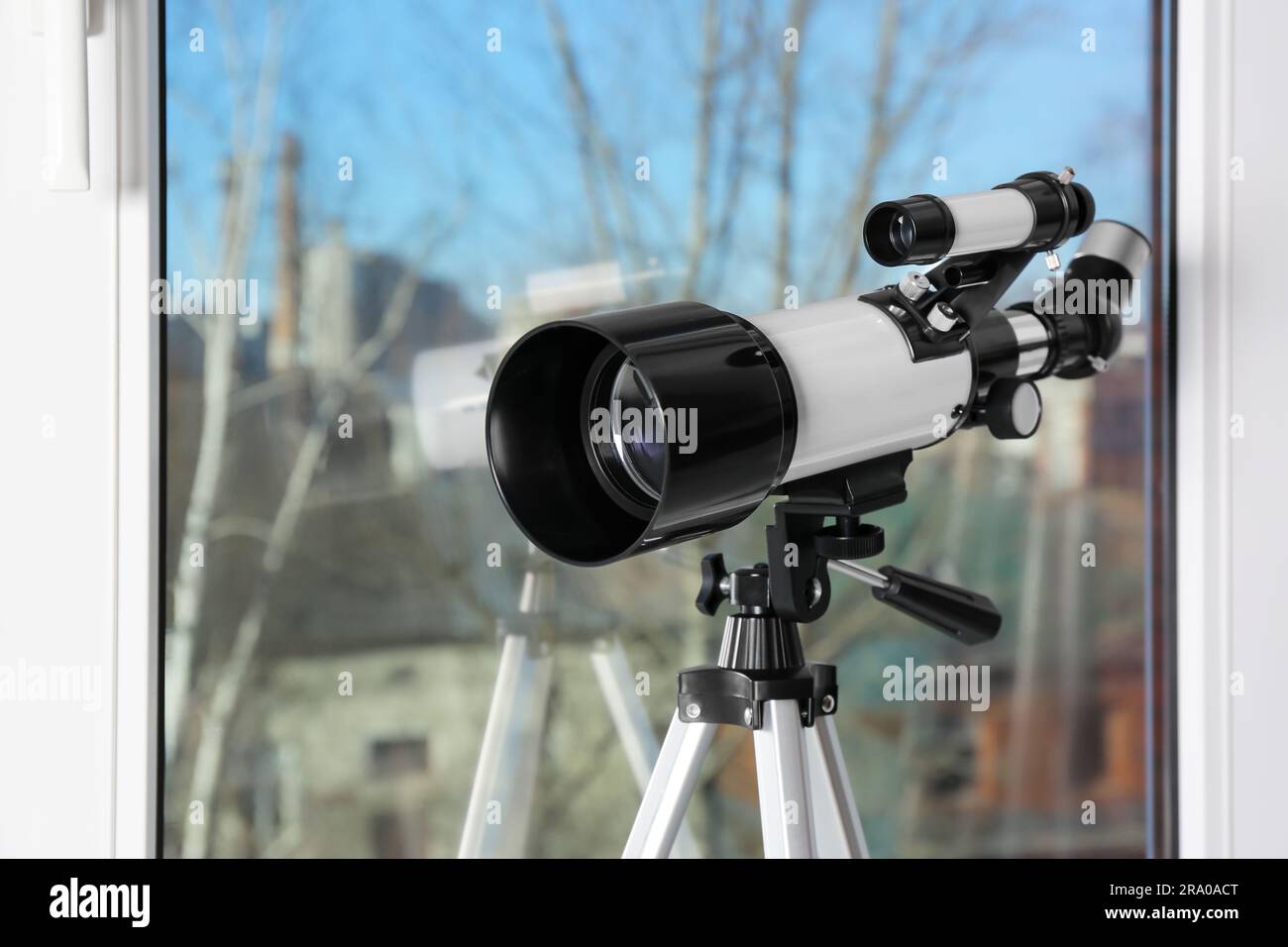 Stativ mit modernem Teleskop in der Nähe von Fenstern im Innenbereich, Nahaufnahme Stockfoto