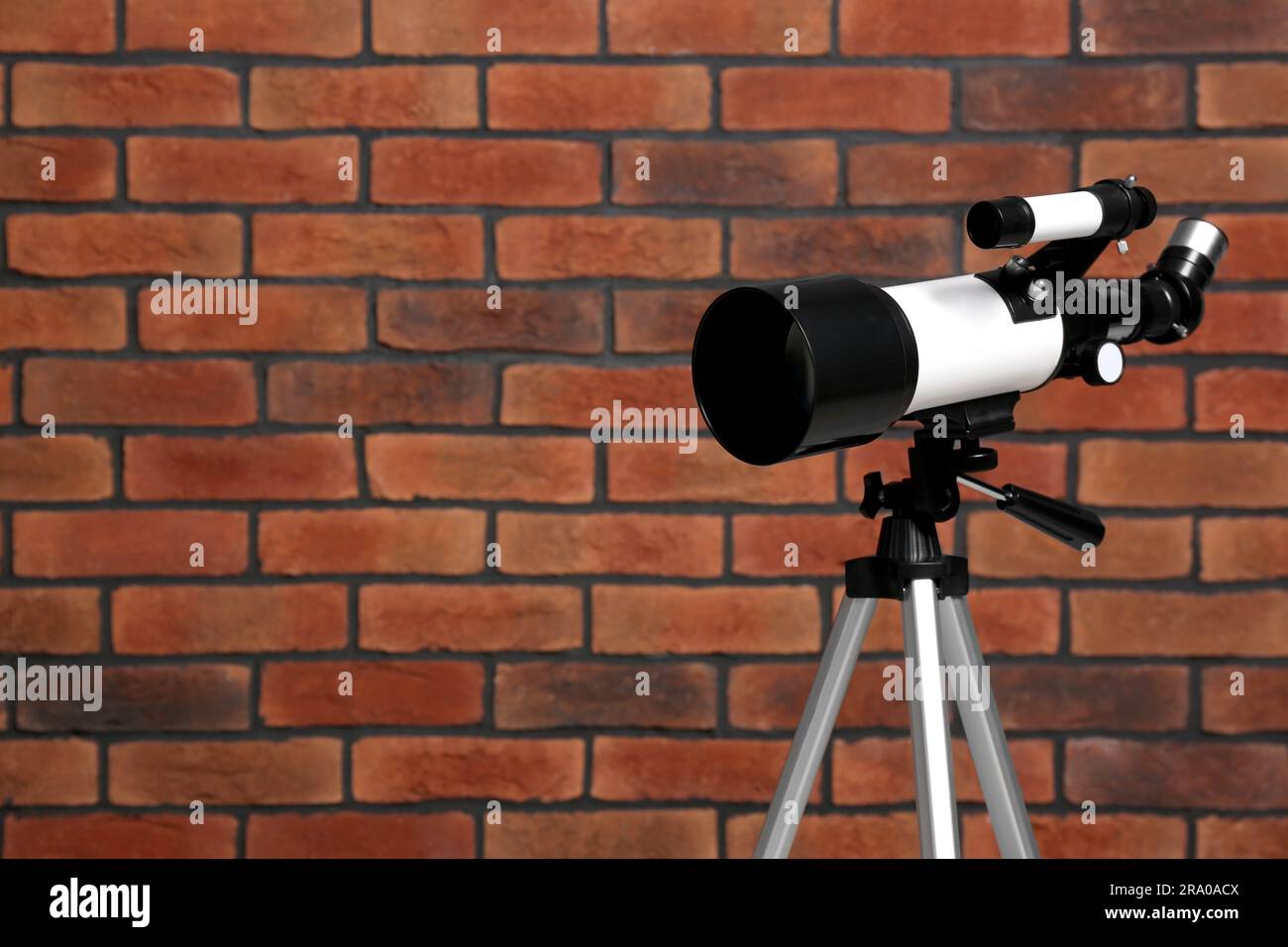 Stativ mit modernem Teleskop nahe der Ziegelwand. Platz für Text Stockfoto