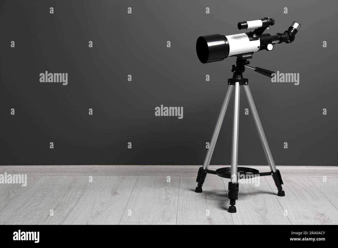 Stativ mit modernem Teleskop nahe der grauen Wand. Platz für Text Stockfoto