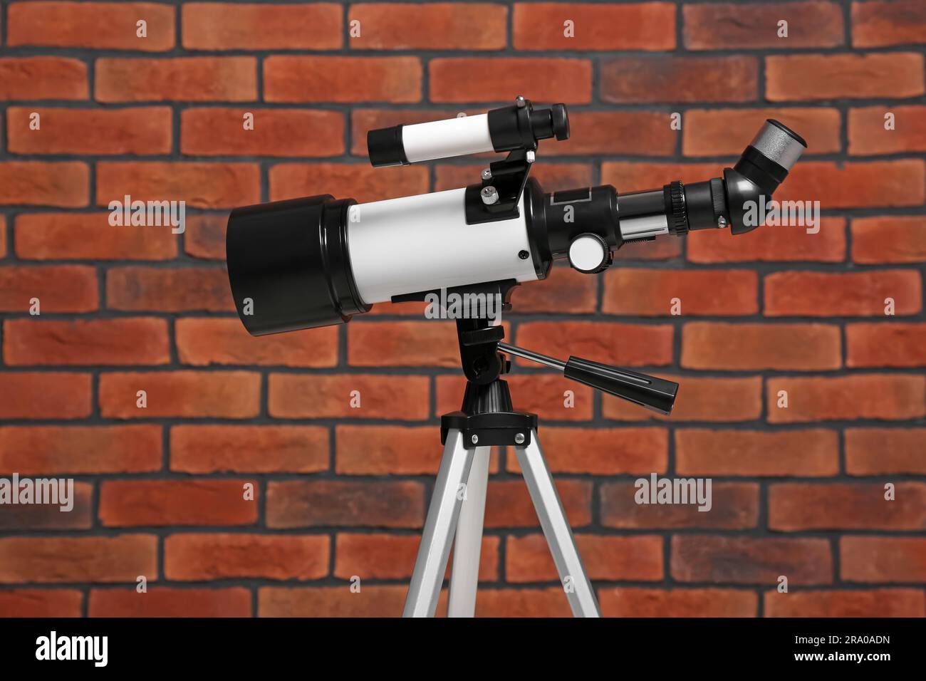 Stativ mit modernem Teleskop nahe der Ziegelwand Stockfoto