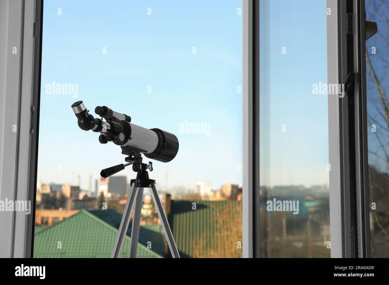 Stativ mit modernem Teleskop in der Nähe offener Fenster im Innenbereich. Platz für Text Stockfoto